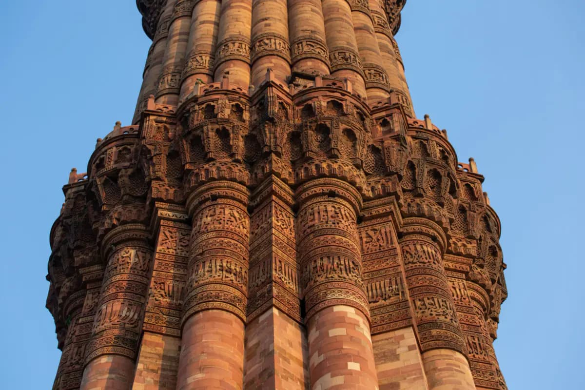 Close view of the Qutb Minar's fluted red sandstone shaft and a balcony, carved with bands of calligraphy, against a blue sky
