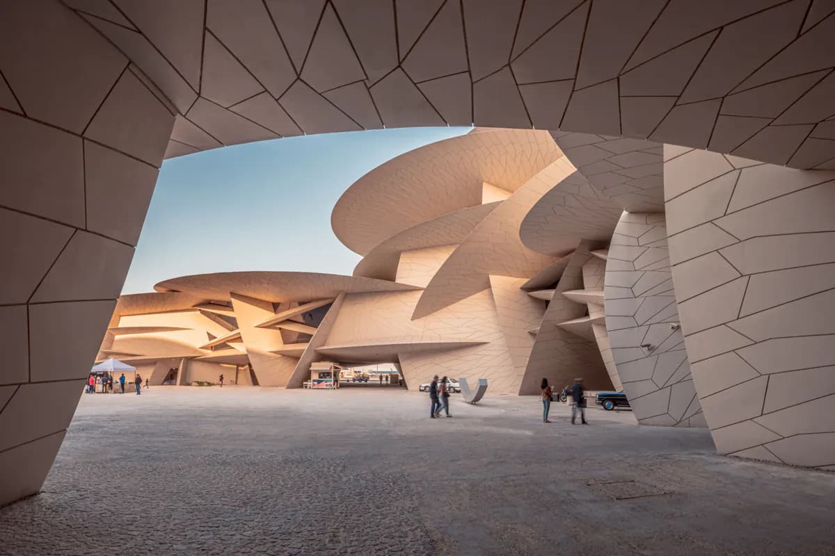 Curved disc shapes of the National Museum of Qatar seen through one of its arches, with visitors on the plaza