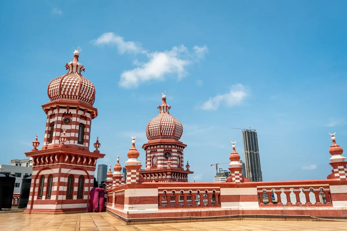 Red and white striped towers and domes on the roof of the Jami Ul-Alfar Mosque, with city towers behind