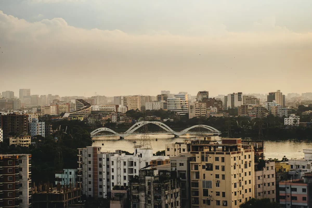 Apartment blocks across Dhaka and white arched bridges over the water, under a hazy evening sky